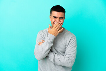 Young handsome man over isolated blue background happy and smiling covering mouth with hand