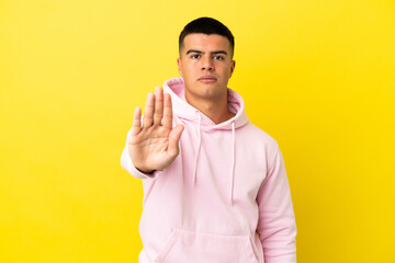 Young handsome man over isolated yellow background making stop gesture