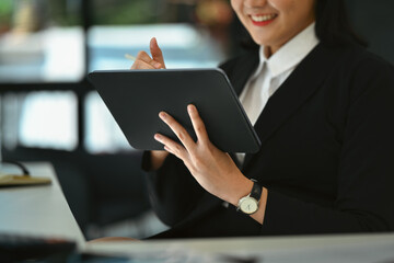 Cropped shot of smiling businesswoman in black suit using digital tablet at her workplace