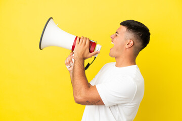 Young handsome man over isolated yellow background shouting through a megaphone to announce...