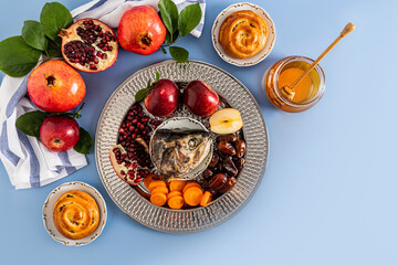 A silver dish with traditional food Rosh Hashanah. pomegranates, apples, honey, fish head, dates....