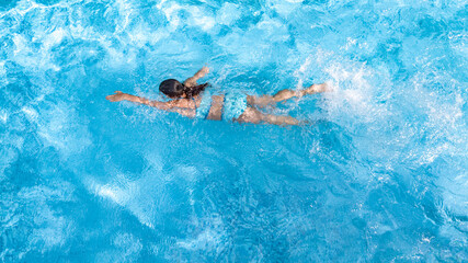 Active girl in swimming pool aerial drone view from above, young woman swims in blue water,...