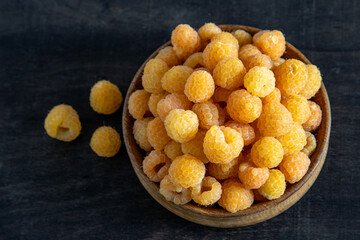 Yellow raspberries in a wooden bowl on the table. Summer berries background. Vitamin food, berry harvest. Healthy nutrition.
