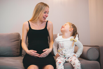 pregnancy photo - pregnant mother with big belly and her daughter happy indoor