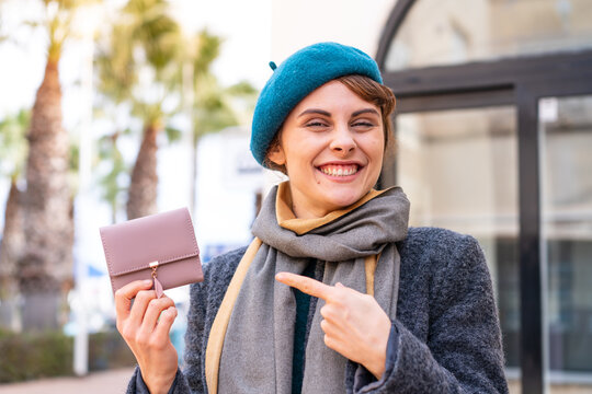 Brunette woman holding a wallet at outdoors and pointing it