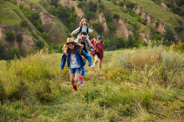 Active parents, man and woman going hiking on trails, hills with their children. Warm summer evening outdoors. Concept of leisure time, fun, nature, active lifestyle, family, travel