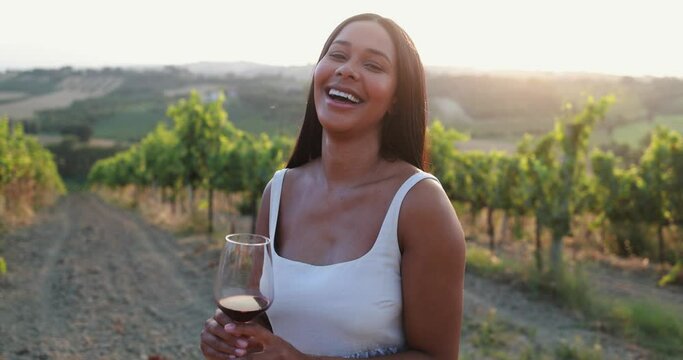 Happy young latin woman smiling in front of camera while holding red wine glass outdoor with vineyards in background - Travel concept