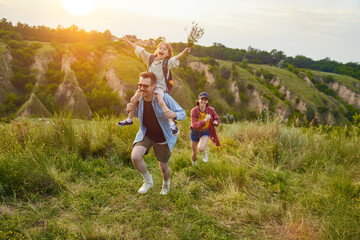 Active parents, man and woman going hiking on trails, hills with their children. Warm summer evening outdoors. Concept of leisure time, fun, nature, active lifestyle, family, travel