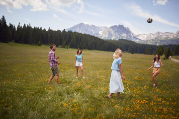 A group of friends is playing with the ball on the meadow at the mountains. Friendship, nature, activity