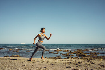 Fototapeta na wymiar a beautiful brunette girl in gray leggings is engaged in fitness on the sand against the background of the sea