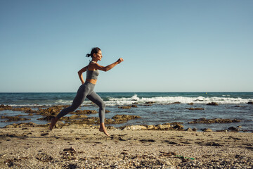 a beautiful brunette girl in gray leggings is engaged in fitness on the sand against the background of the sea