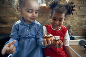 Close up portrait shot of two little girls messy eating muffins in kitchen together, feeling happy. - Powered by Adobe