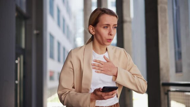 Businesswoman reading news on mobile phone and feels bad having breathing problems, chest pain, panic attack outdoors. Business woman female manager touches chest. Heart attack, problem health.