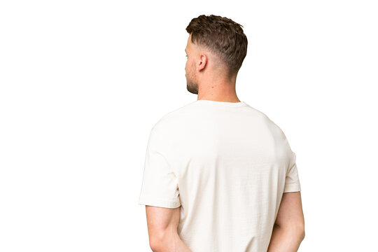 Young blonde caucasian man over isolated background in back position and looking back
