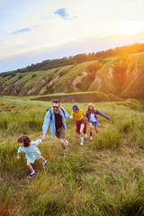 Parents going hiking with their children, daughters on warm summer evening. Beautiful hills...