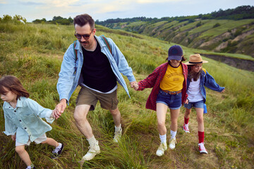 Loving, caring family, man and woman going hiking with their children. Walking on trails, hills, fields Beautiful summer nature landscape. Concept of leisure time, fun, nature, active lifestyle