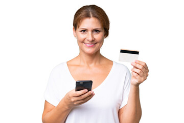 Fototapeta premium Middle-aged caucasian woman over isolated background buying with the mobile with a credit card
