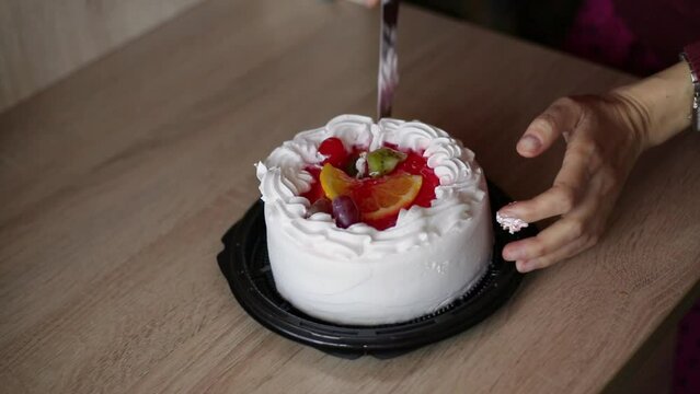 woman's hands cut off piece of delicious fruit cake with cream.