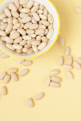 Macro photo of white beans in white plate and scattered on a beige or yellow background top view