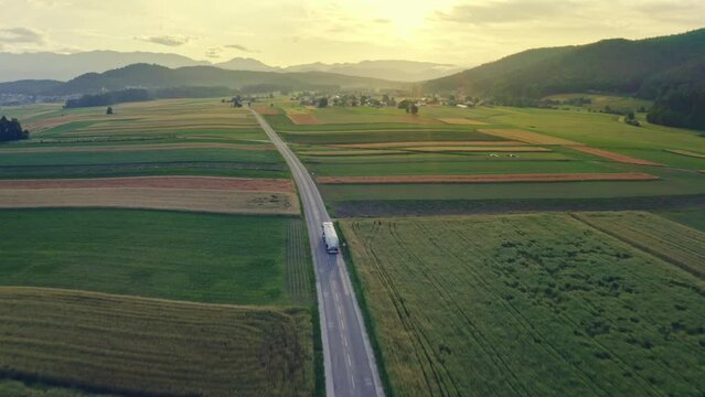 Lorry truck driving along countryside highway, transporting liquid cargo aerial view tracking shot. Oil tanker riding on road at sunset with mountains on horizon