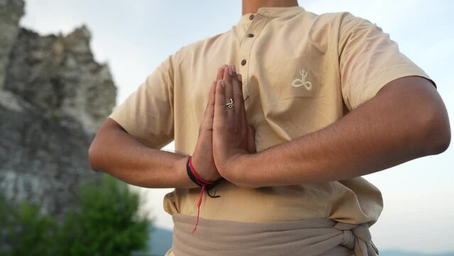 Meditating with hands in hatha yoga position at sunrise on top of the hill by an unrecognizable Indian person