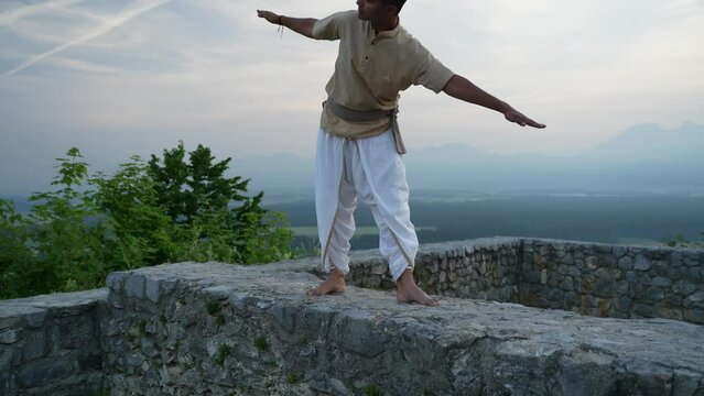 Man rising from hatha yoga pose on top of the hill with castle ruins at sunrise