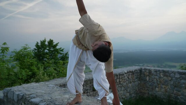 Yoga pose at top of the hill surrounded with fields and trees at dawn on stone wall