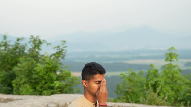 deeply focused young Indian male meditating in hatha yoga pose with sun reflecting on his brown skin at sunrise in hearth of nature on top of the hill