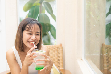Obraz na płótnie Canvas Young Asian woman smiling with apple soda, A woman holding a glass of apple soda with feeling happy and enjoy to eat food in the restaurant. Enjoy eating, refreshing summer drinks, Taste concept.