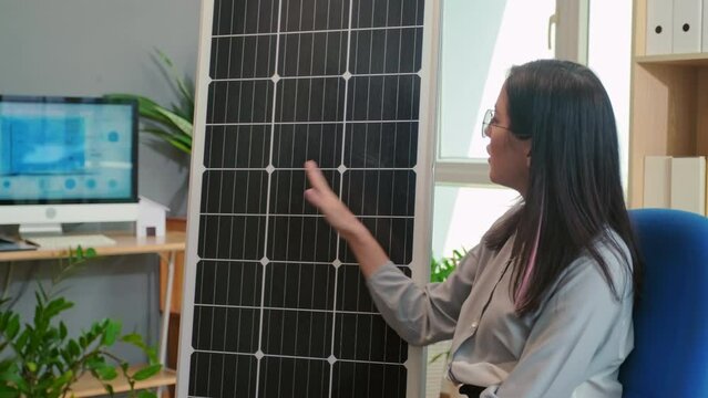 Medium shot of female sales manager showing clients advantages of using solar power on solar panel while sitting at office