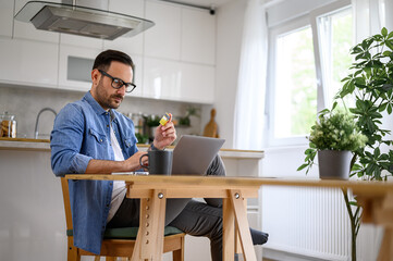 Serious young businessman paying through credit card while shopping online on laptop in home office