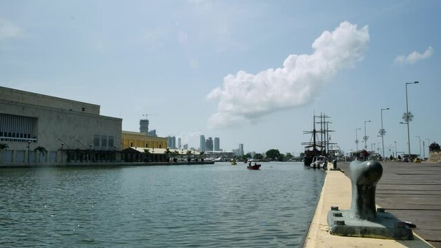Cartagena quay with motorboat, galleon, distant skyscrapers. Wide dolly.