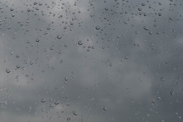 Blurred image of raindrops on glass against a gray sky.