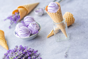 Creamy vegan purple ice cream balls in a bowl with lavender flowers, waffle cones on a gray...