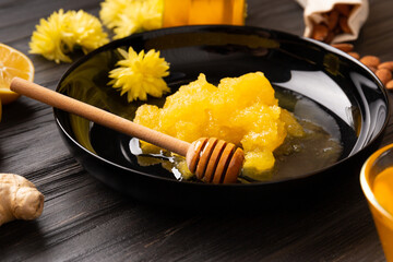 Crystallized honey in a black plate with dipper on a dark wooden background.