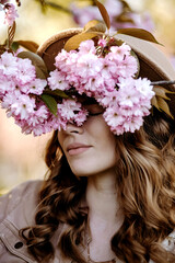 Naklejka premium Young girl with hat in a sakura garden
