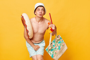 Confused puzzled funny man wearing shorts swimsuit and panama holding donut rubber ring isolated on...