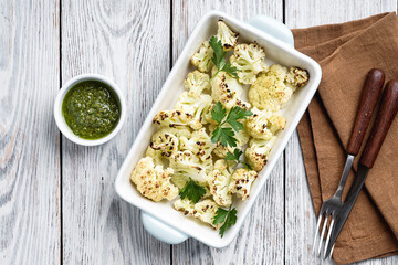 Roasted white cauliflower with pesto sauce on rustic wooden table