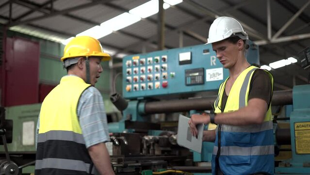 group of two diversity caucasian industrial Engineer manager man discussion with asian mechanic worker man using tablet checking machinery in industry manufacturing  factory. looking watch time clock