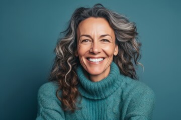 Fototapeta premium Close-up portrait photography of a happy mature woman wearing a cozy sweater against a teal blue background. With generative AI technology