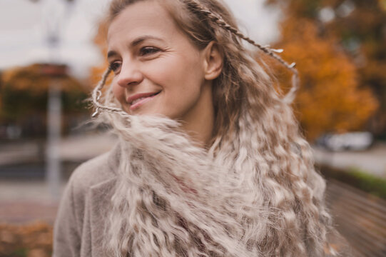Attractive middle-aged blonde with pigtails in trendy clothes shakes her head and her hair develops. Mature woman enjoys autumn. Motion in blur, selective focus