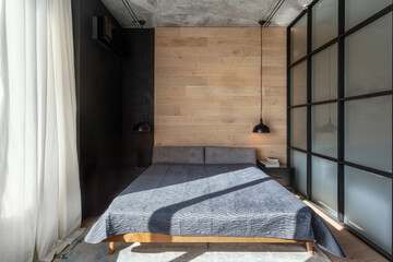 Comfortable double bed with bedcover against wooden wall in bedroom