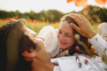 Obraz premium The close portrait of wedding couple laying at the poppies field laughing smiling