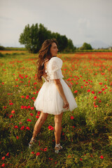 Stylish brunette bride in short white wedding dress posing in half turn at the red poppies field 