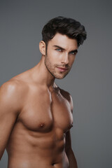 Fototapeta premium Charismatic close-up of a shirtless brunette model with a fit and toned physique against a modern gray backdrop