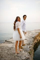 Stylish bride in short wedding dress and groom walking at old stone Italian pier and smiling 