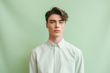 Obraz premium Medium shot portrait photography of a beautiful boy in his 20s wearing an elegant long-sleeve shirt against a pastel green background. With generative AI technology