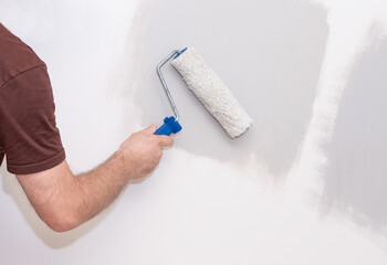 The male hand of the painter, holds a paint roller on the background of the wall.