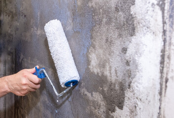 The male hand of a painter, holds a paint roller and applies a primer to the wall.