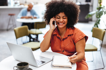 Business woman talking on the phone, communicating with her clients as she works in a cafe